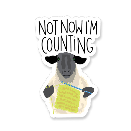 Sticker with a sheep holding yarn and a crochet hook with text 'Not Now I'm Counting' on a white background.