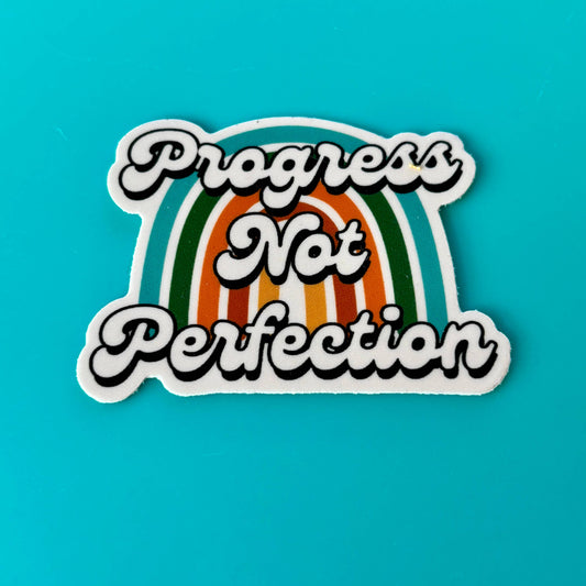 Sticker with 'Progress Not Perfection' text on a rainbow design against a blue background